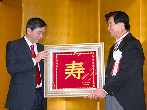ベトナム ビンディン省人民委員会副知事トラン・チャウ氏（左）からお祝いの品が加藤均理事長に贈られた