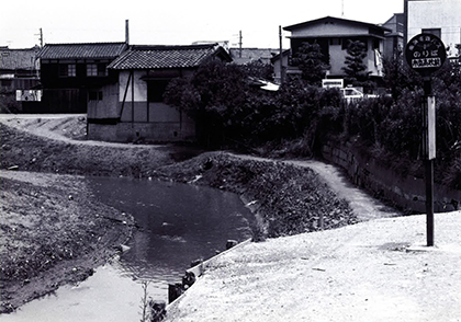 土居川南東部の曲がり角（昭和30年代）
飛び越えられるほどの細い川となり、護岸もない。
バス亭の表示に、今はない堺市立高校の表示がある（現在共同住宅として再建設中）。大仙西町２丁